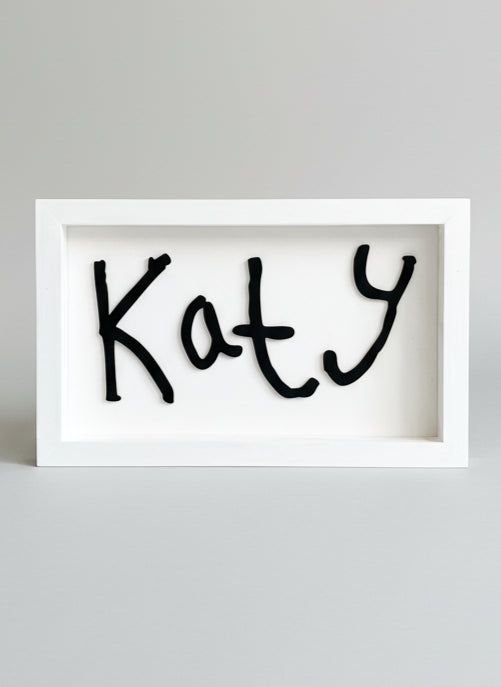 Framed artwork with the name 'Katy' in black ink on a white background