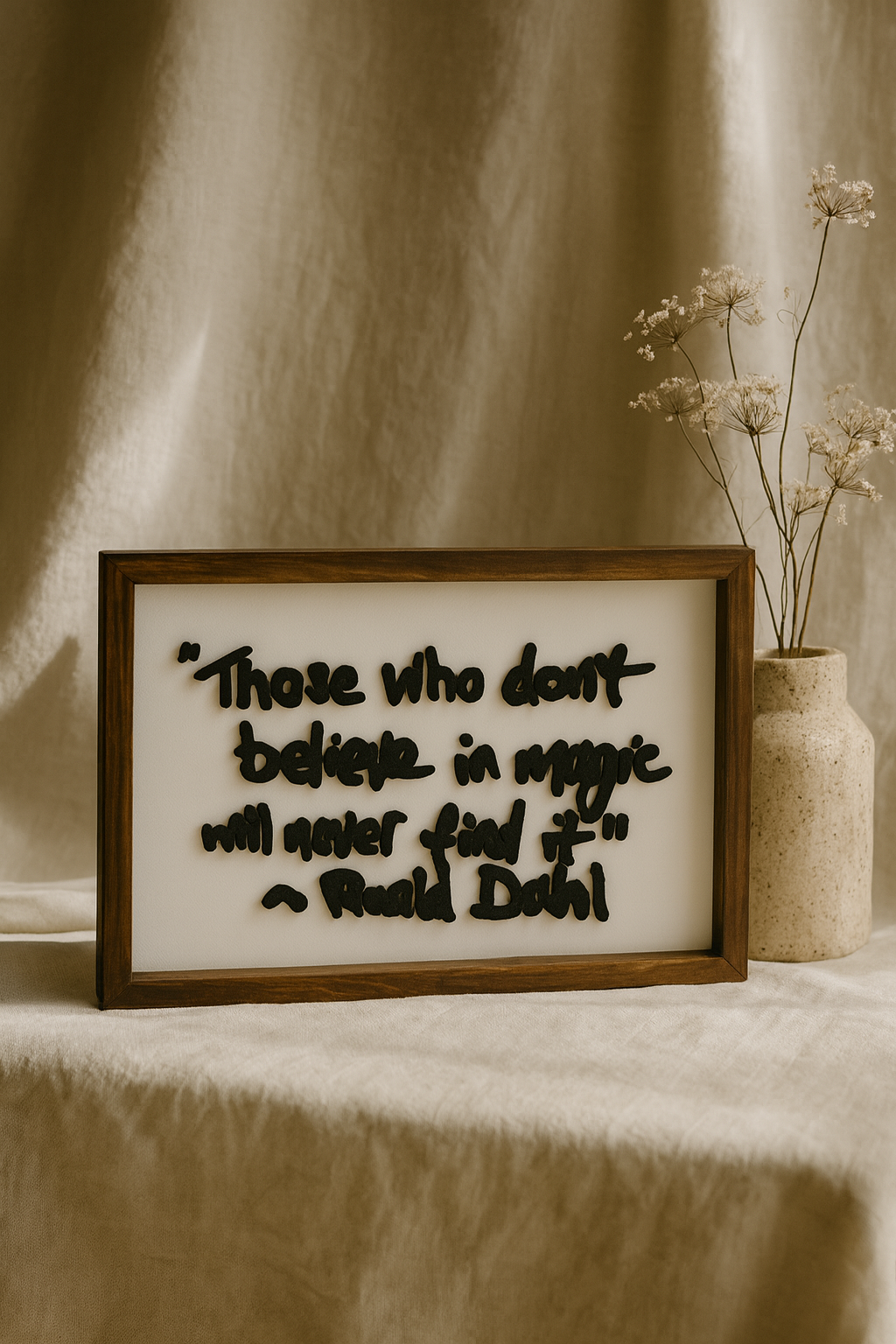 Framed quote by Roald Dahl on a table with a vase of flowers.