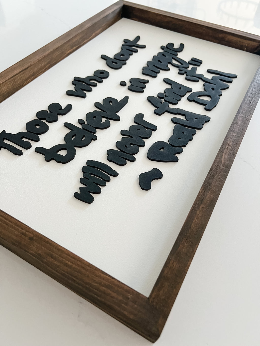 Wooden frame with black cut-out letters spelling a motivational quote on a white background